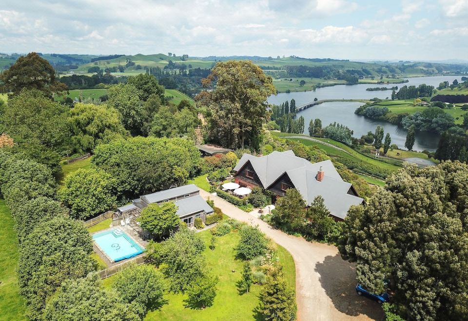 aerial view of a large house surrounded by trees and a body of water , with a swimming pool in the yard at Lake Karapiro Lodge