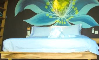 a bed with a blue headboard is in a room with wooden floors and a large blue flower mural on the wall at The Happy 8 Retreat @ Kuala Sepetang