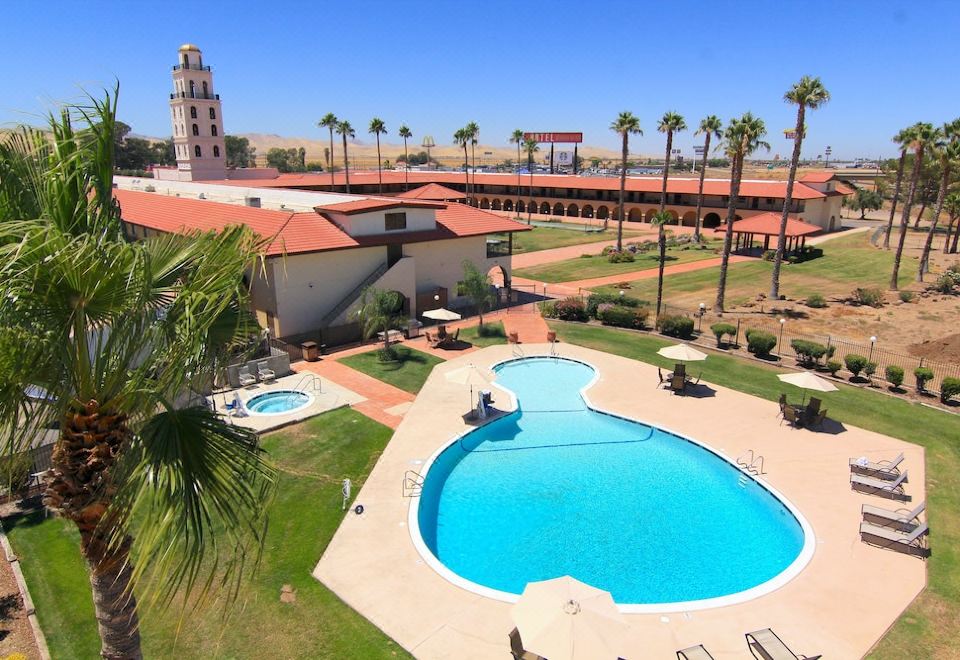 an outdoor swimming pool surrounded by grass and palm trees , with a building in the background at Hotel Mission de Oro