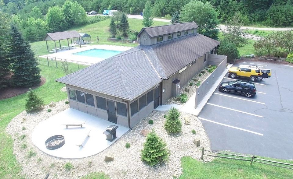 a large , modern building with a wrap - around porch and multiple windows , surrounded by a parking lot and a swimming pool at Rock House - Hocking Hills
