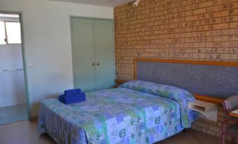 a bed with a blue blanket and a blue suitcase on top of it , next to a brick wall at The Lodge Motel