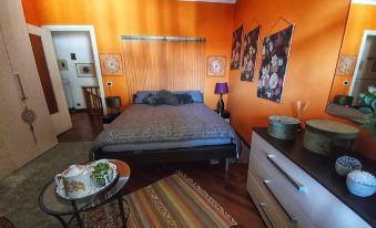 a bedroom with an orange wall , a bed , and a dresser , along with various items on the table at CasAda