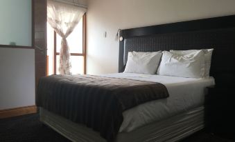 a large bed with a black headboard and white sheets is in a room with a window at Hotel Savera