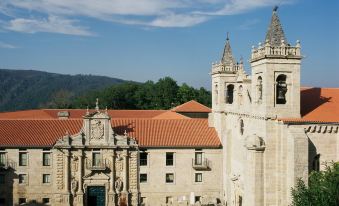 a large stone building with a red roof and two towers , situated in a grassy field at Parador de Santo Estevo