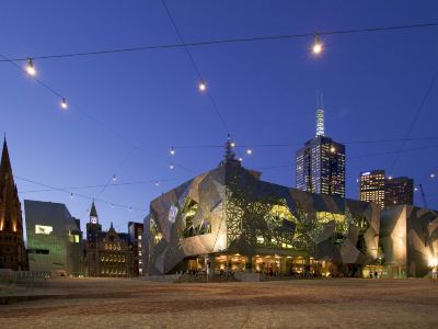 a modern building with a unique design is lit up at night , surrounded by other buildings and a street at Ibis Melbourne Hotel and Apartments