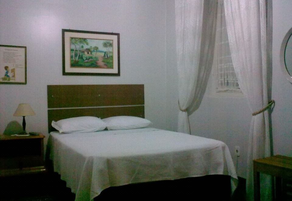 a bed with a white sheet and two pillows is in a room with a painting on the wall at Hotel Brasil