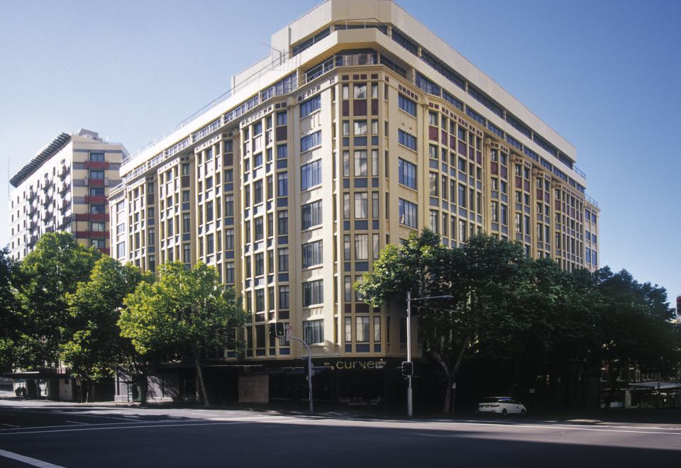 a large , yellow building with many windows is situated on a city street in front of a modern cityscape at Vibe Hotel Sydney