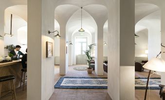a hallway with white walls and arched ceilings leads to a living room with a couch , potted plant , and hanging light fixtures at São Lourenço do Barrocal