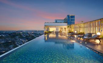 a large swimming pool is situated on the edge of a rooftop pool , with a city view in the background at Hotel Ciputra Cibubur Managed by Swiss-Belhotel International