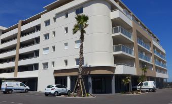 a modern apartment building with white balconies and palm trees , surrounded by cars parked in the parking lot at Balnea