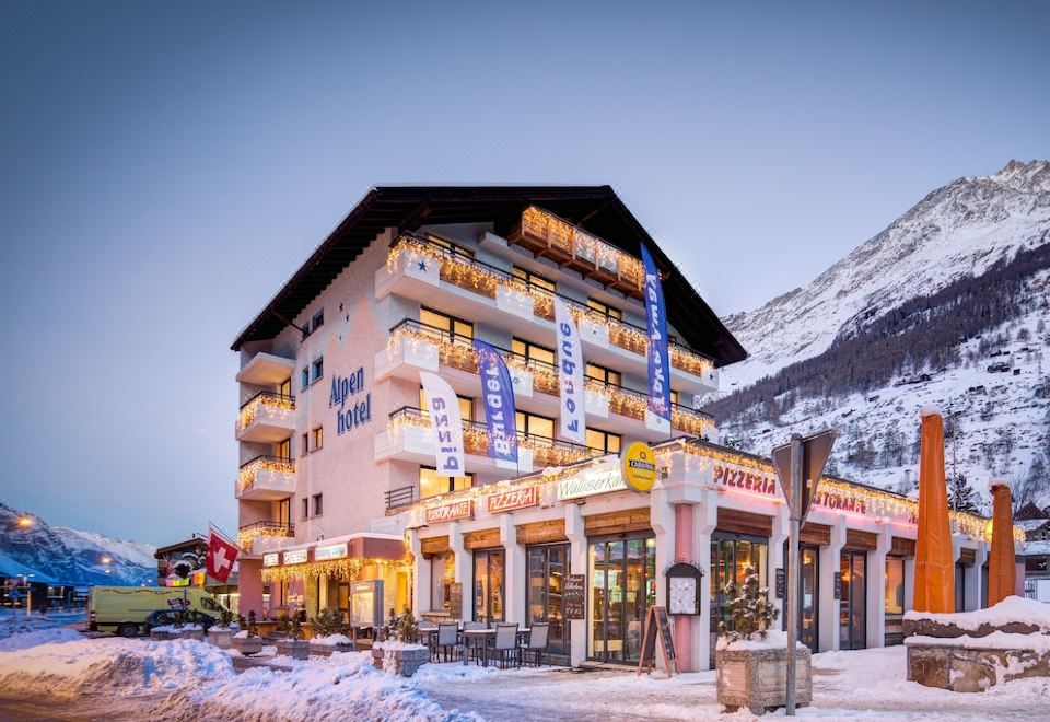 a snowy mountainous landscape with a hotel building in the background , surrounded by trees and other buildings at Matterhorn Inn