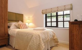 a neatly made bed with white linens and a beige comforter is situated in a bedroom next to a window at Barton B&B