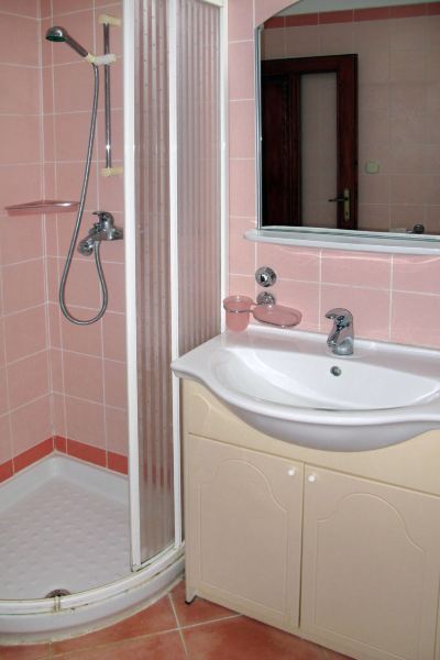 a bathroom with pink tiled walls , a shower , and a white sink on a beige cabinet at Ingrid