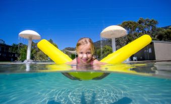 a young girl is swimming in a pool with a yellow float above her head at Nrma Halls Gap Holiday Park