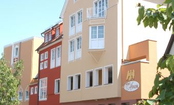 a red and yellow apartment building with balconies , surrounded by trees and a blue sky at Hotel Adler - Paulas Alb