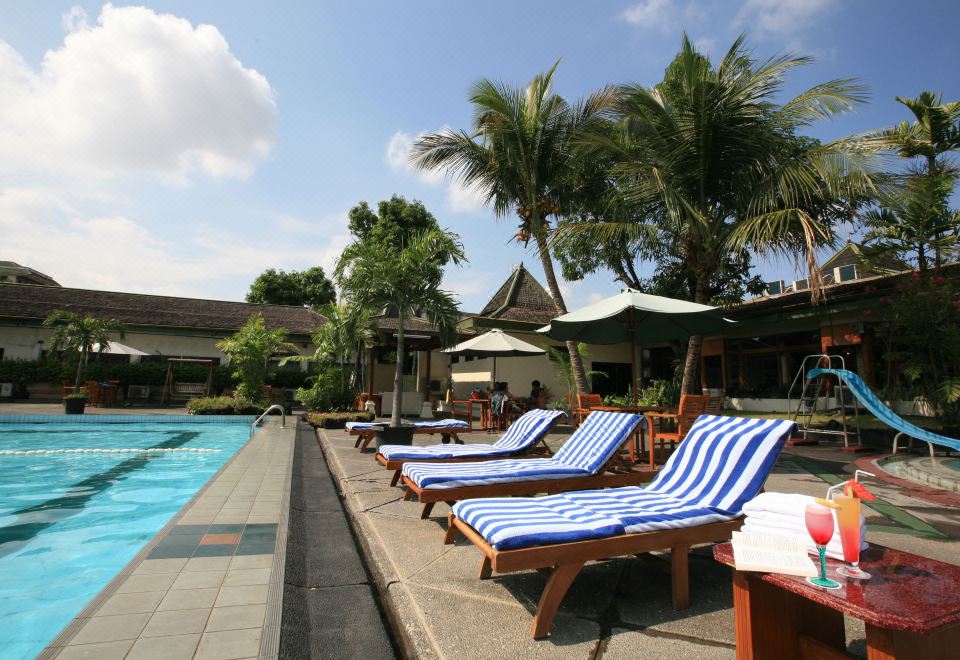 a resort with a large pool surrounded by lounge chairs and umbrellas , providing a relaxing atmosphere at Kusuma Sahid Prince Hotel Solo