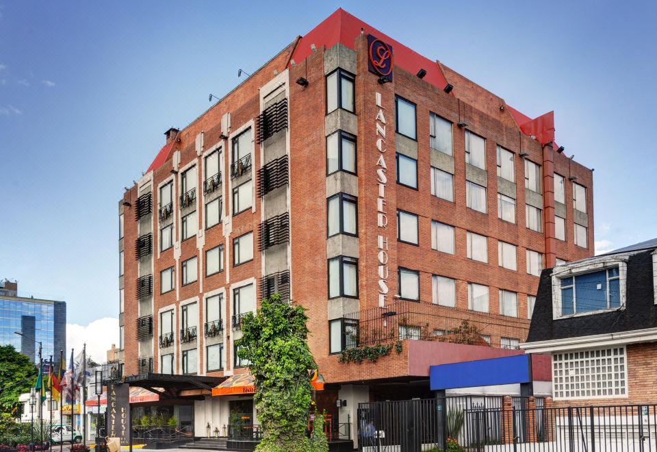 a large brick building on a city street , with a hotel in the background surrounded by trees and other buildings at Lancaster House