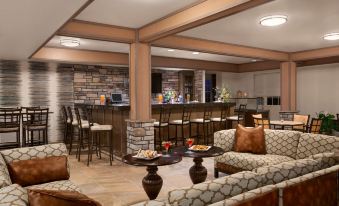 a well - lit bar area with several chairs and couches arranged around it , creating a cozy atmosphere at Hyatt House Minot