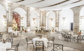 a large white building with arched ceilings and columns , featuring tables and chairs set up for dining at Parador de Zafra