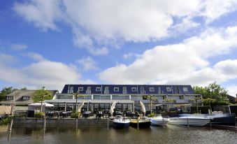 a building with a blue roof is next to a dock where several boats are docked at Fletcher Hotel Restaurant Loosdrecht-Amsterdam