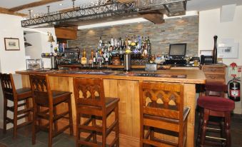 a wooden bar with several stools and chairs , as well as various bottles and glasses on the counter at The Hood Arms