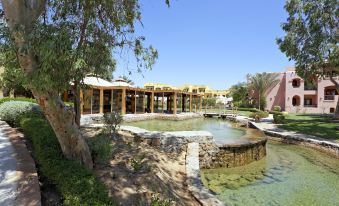 a beautiful outdoor area with a pool , umbrellas , and a wooden structure surrounded by trees at Three Corners Rihana Resort El Gouna