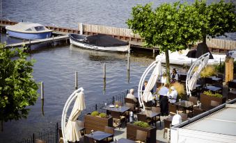 a restaurant patio overlooking a body of water , with tables and chairs set up for dining at Fletcher Hotel Restaurant Loosdrecht-Amsterdam