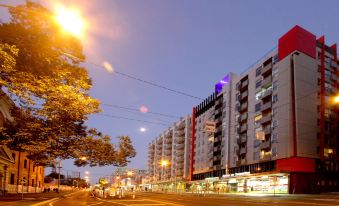 a city street at night with tall buildings and colorful lights , reflecting the city 's vibrant atmosphere at Arrow on Swanston