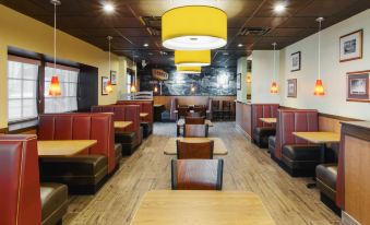 a restaurant with wooden tables and chairs , a red booth , and a yellow light fixture at Best Western Plus Carriage Inn