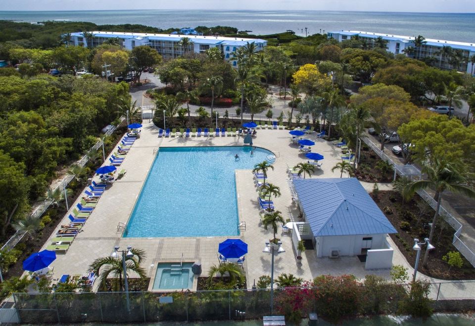 a resort with a large pool surrounded by lounge chairs , umbrellas , and palm trees , as well as a view of the ocean in the background at Ocean Pointe Suites at Key Largo