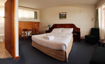 a large bed with white linens and a wooden headboard is in a room with a desk , chair , and window at City View Motel