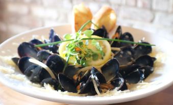 a plate of mussels and a lemon wedge garnished with parsley and a garlic clove at Inn on the Lakes