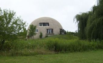 a modern dome - shaped house surrounded by lush green grass and trees , with a cloudy sky in the background at Thyme for Bed