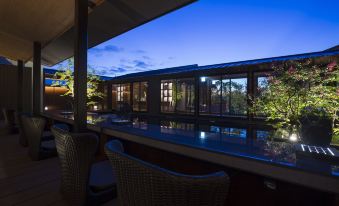 a patio area with a table and chairs , overlooking a pool , and the sky is blue at night at Biwako Ryokusuitei