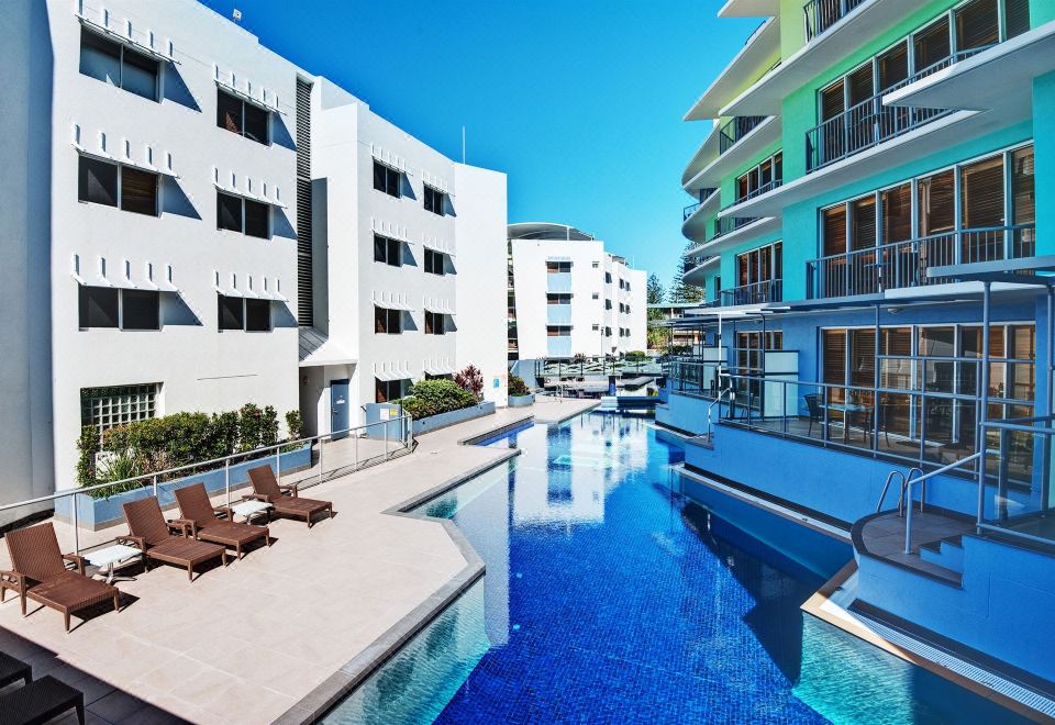 a modern apartment complex with a swimming pool surrounded by white buildings , providing a relaxing atmosphere at Rolling Surf Resort Sunshine Coast