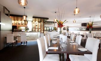 a large dining room with white chairs and tables , and pendant lights hanging from the ceiling at Dog Rock Motel