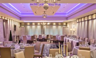 a well - decorated banquet hall with multiple tables set for a formal dinner , each table having its own arrangement of chairs and cutlery at Ingliston Country Club Hotel