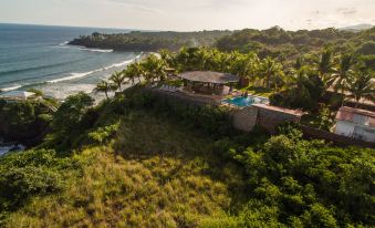 a luxury house with a pool is situated on a hillside overlooking the ocean , surrounded by lush greenery at Hotel Miraflores
