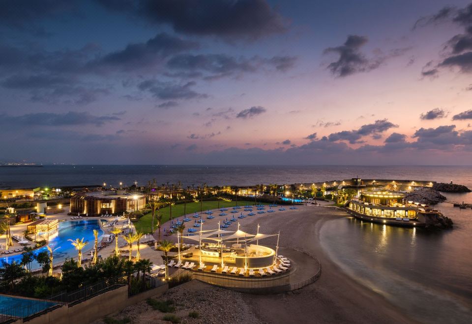 a beautiful beach scene at dusk , with a large pool and the sun setting in the background at Kempinski Summerland Hotel & Resort Beirut