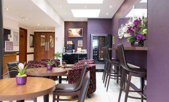 a restaurant with purple walls , wooden tables and chairs , and a counter with a bottle of wine at Hello Hotel