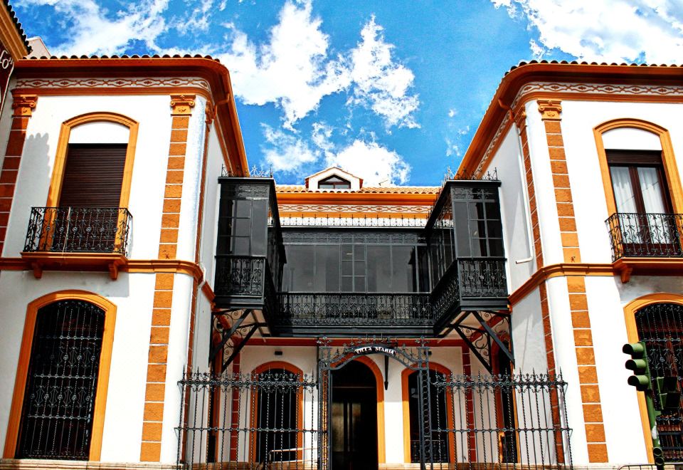 a large , two - story building with orange and white walls and black balconies , under a blue sky with white clouds at Hotel Villa Maria
