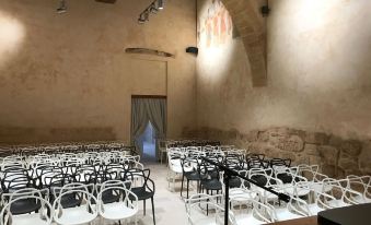 an empty conference room with rows of white and black chairs , a stage at the end , and a large window at Castello di Ugento