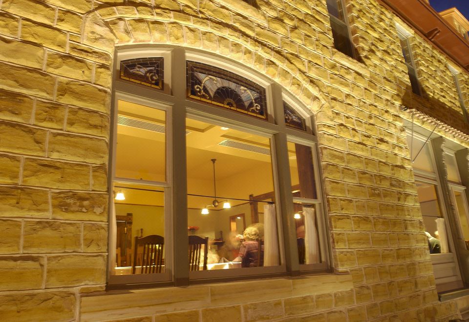 a brick building with a large window that offers a view of the outside , while people are sitting at the window at Midland Railroad Hotel