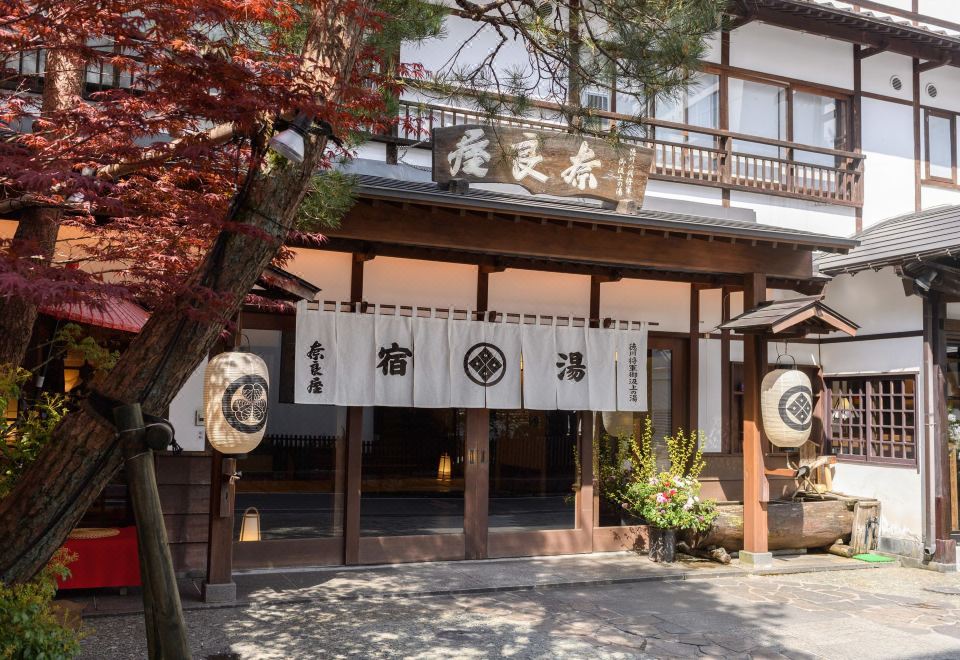 a traditional japanese house with a wooden sign on the front , surrounded by trees and plants at Naraya