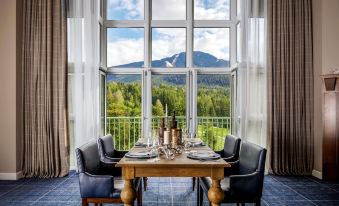 a dining table is set with plates , wine glasses , and a vase in front of a large window overlooking a mountain at Fairmont Chateau Whistler