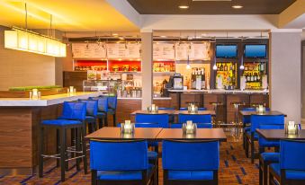 a modern restaurant with blue chairs and tables , a bar area , and a variety of food items on display at Courtyard Richmond Northwest/Short Pump