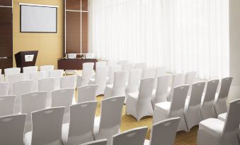 a large conference room with rows of white chairs arranged in a semicircle , and a projector mounted on the wall at Courtyard Kochi Airport