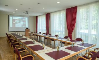 a conference room with long tables , chairs , and red curtains , ready for a meeting or presentation at Glockenhof
