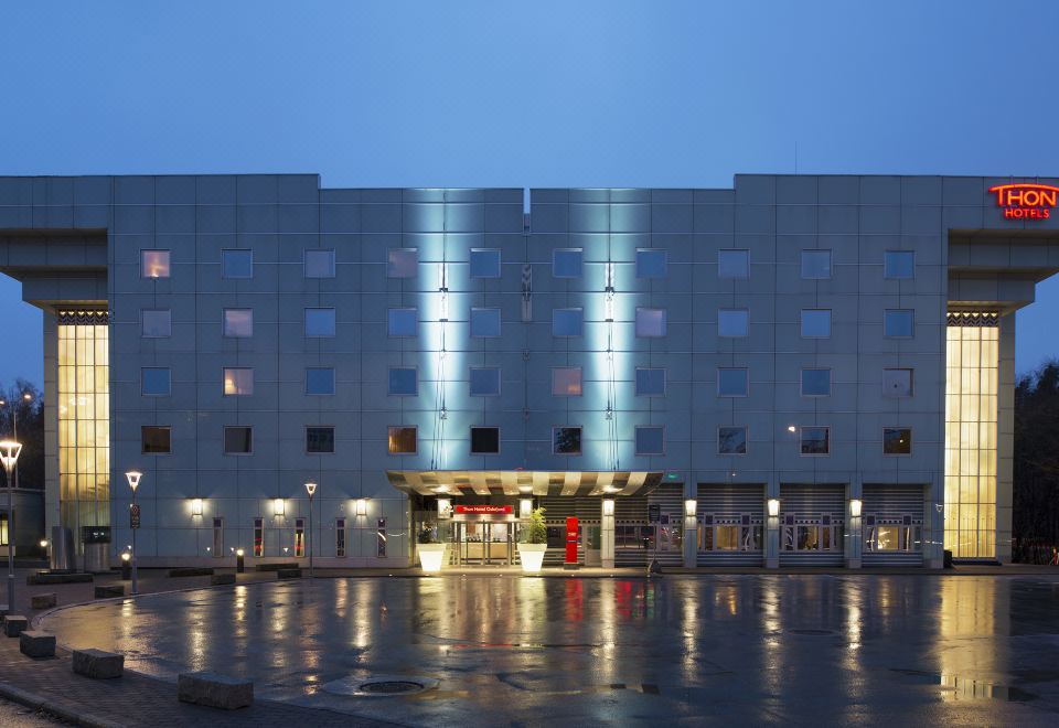 a modern building with a large glass facade and two towers , illuminated at night against the dark sky at Thon Hotel Oslofjord