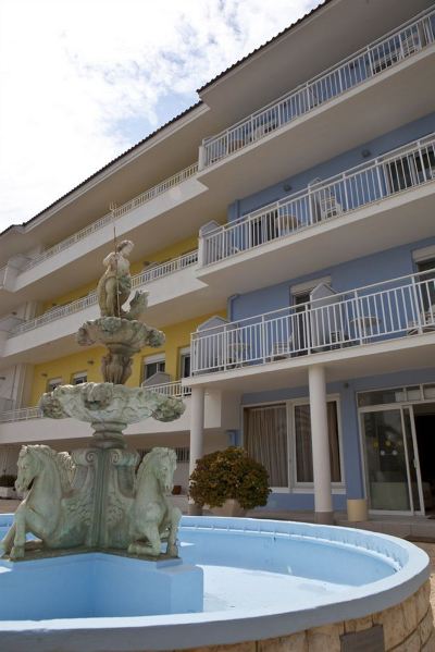 a white building with multiple balconies and a fountain in front of it , surrounded by trees at Hotel Summery